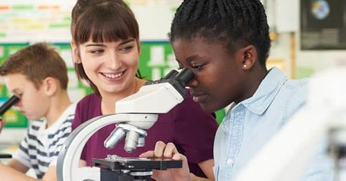 A student in a blue shirt looking through a microscope.